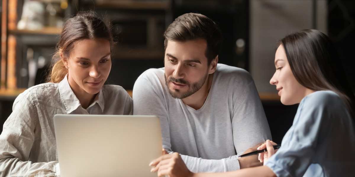 A young couple sitting at a table and smiling while reviewing financial charts and documents with a professional female advisor.
