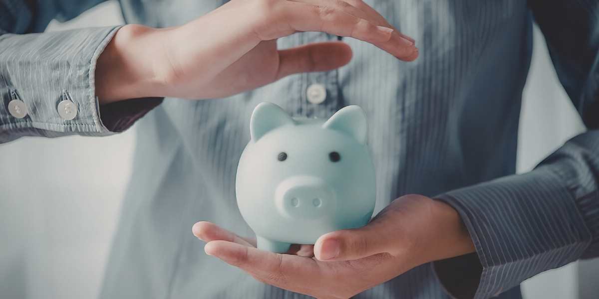 A person holding a small blue piggy bank with their other hand forming a protective arch over it, symbolizing small deposit options and savings strategies for a commercial mortgage.