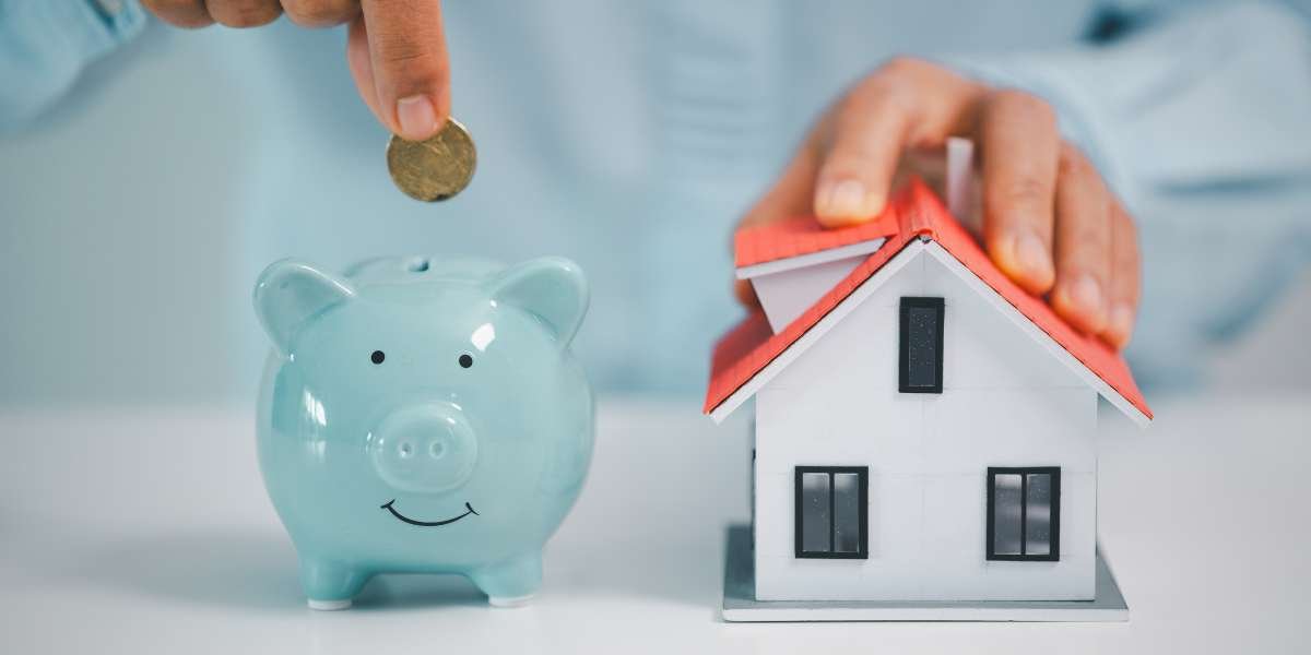 A close-up of a person putting a coin into a blue piggy bank next to a small model house, illustrating deposit requirements and mortgage rates in 2026.
