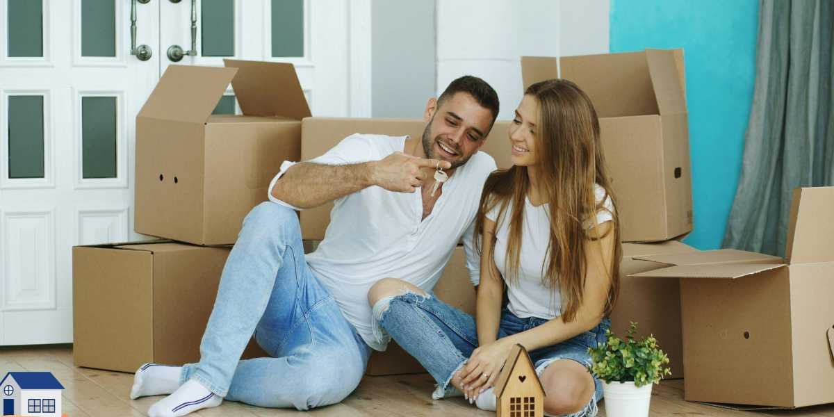 A happy young couple sitting on the floor of their new home surrounded by unpacked cardboard boxes, with the man smiling and holding up the keys to the house.