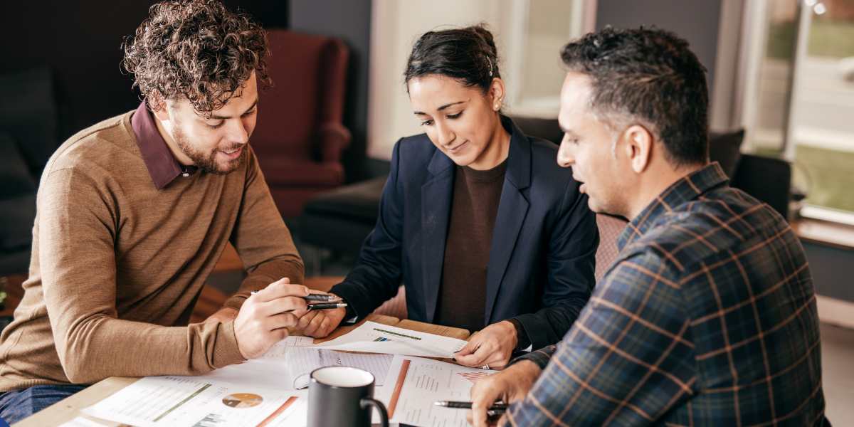 A group of startup business owners reviewing financial documents and charts on a table during a meeting with a commercial mortgage advisor in a modern office.