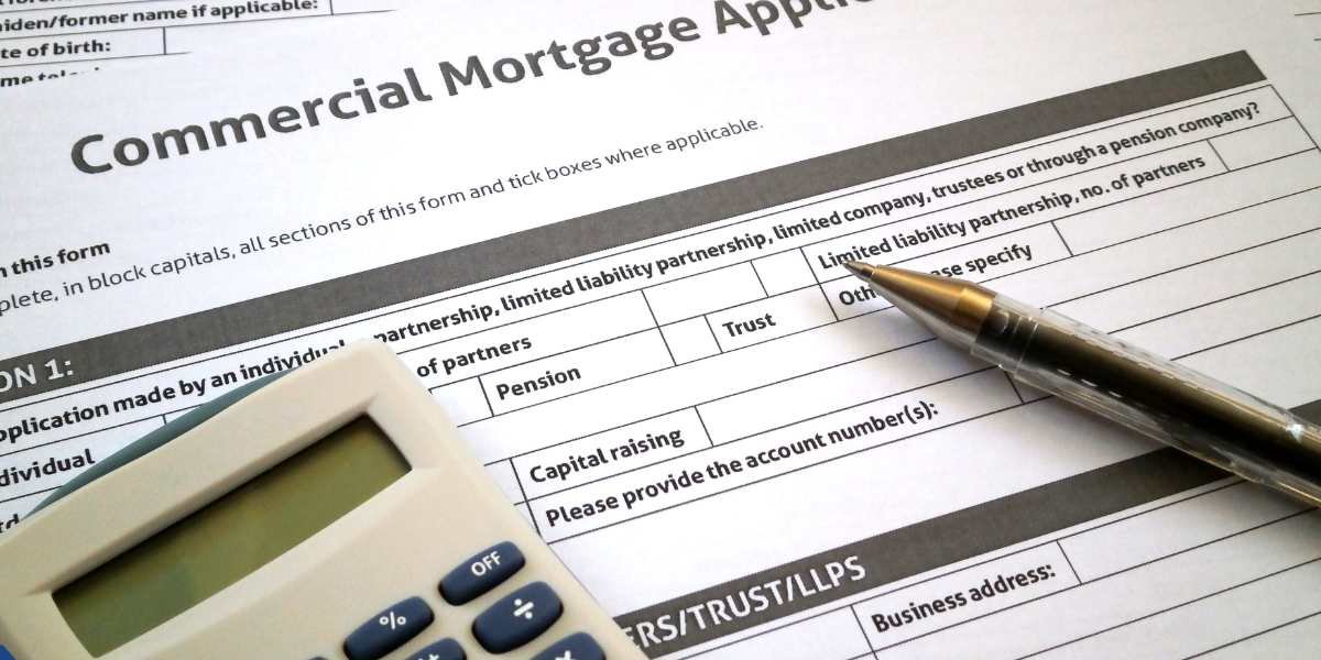 A close-up of a printed Commercial Mortgage Application form on a desk, with a silver pen and a calculator resting on top to calculate business startup mortgage costs.