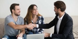 A young couple shaking hands with a mortgage advisor or broker during a meeting, representing first-time landlords securing a buy-to-let mortgage in the UK.