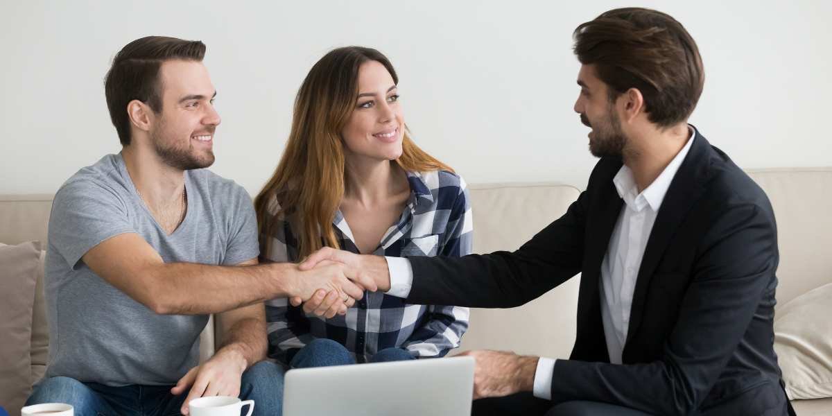 A young couple shaking hands with a mortgage advisor or broker during a meeting, representing first-time landlords securing a buy-to-let mortgage in the UK.
