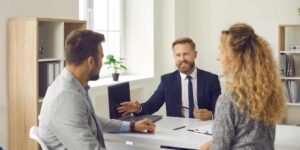 A bearded professional mortgage advisor in a suit explaining loan criteria and company profits on a laptop to a couple applying for a UK limited company director mortgage.