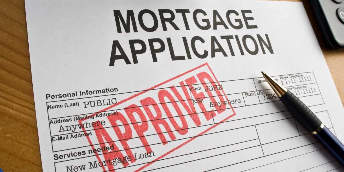A close-up of a paperwork form titled "Mortgage Application" lying on a wooden surface, clearly stamped with a large red "APPROVED" ink mark diagonally across the personal information section, with a black and gold pen resting beside it.