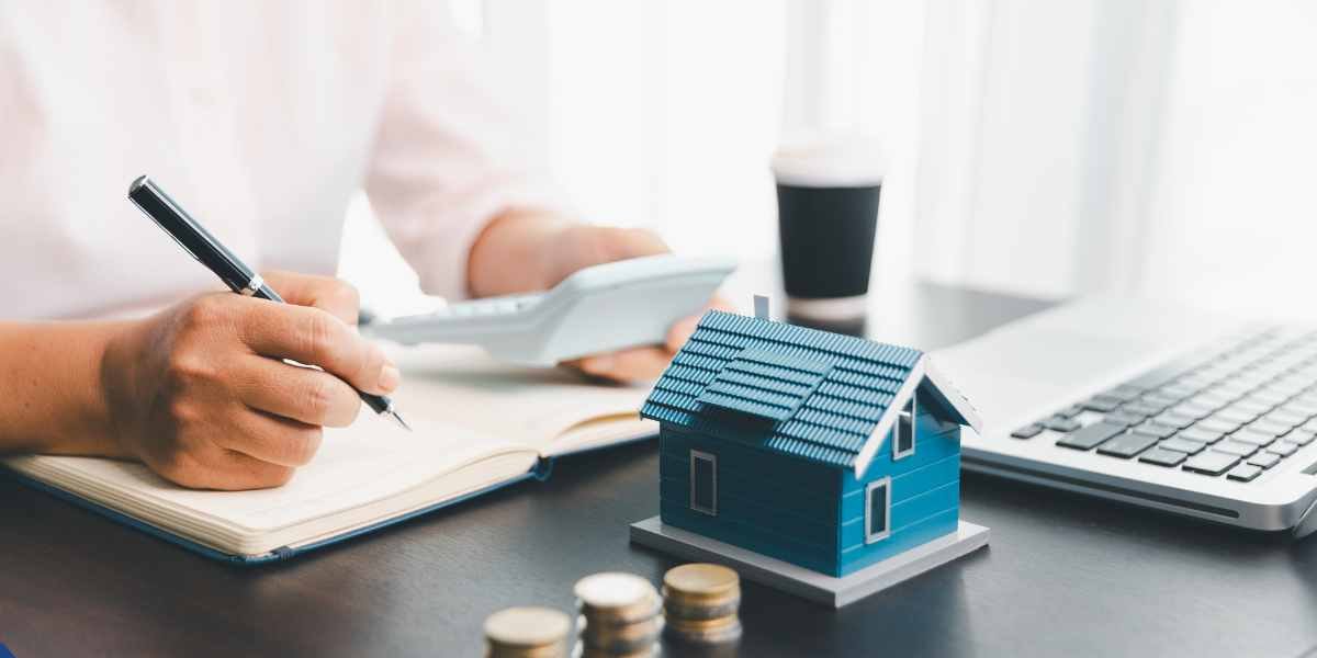 A financial professional using a calculator and reviewing documentation next to a small house model to assess a limited company director's salary and dividend income for a mortgage application.