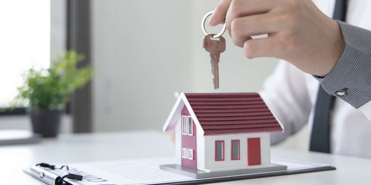 A close-up of a mortgage lender or broker holding a house key over a miniature model home sitting on a clipboard, symbolizing mortgage approval and property ownership for self-employed applicants.