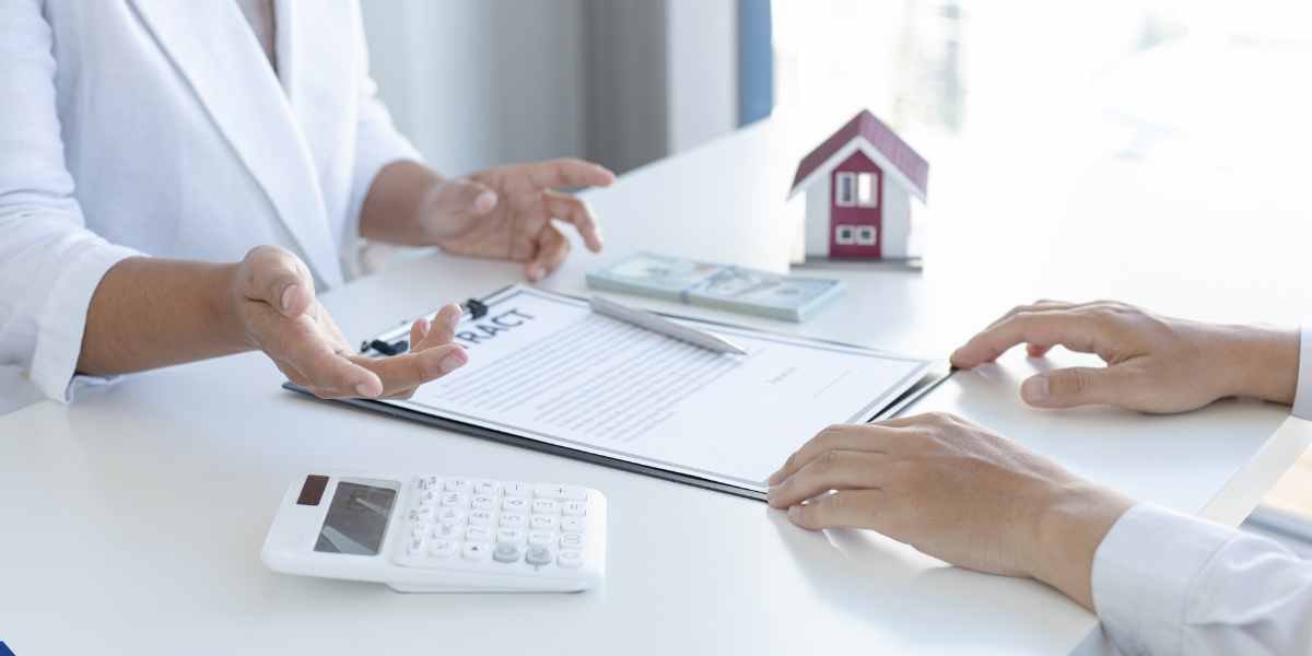 Close-up of an advisor explaining a debt consolidation mortgage contract to a client, with a calculator, cash stack, and small house model on a white desk.