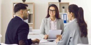 A female mortgage broker smiling as she reviews documents with a couple in an office, illustrating expert guidance for borrowers trying to navigate UK bad credit mortgage options.