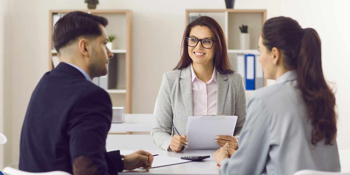 A female mortgage broker smiling as she reviews documents with a couple in an office, illustrating expert guidance for borrowers trying to navigate UK bad credit mortgage options.