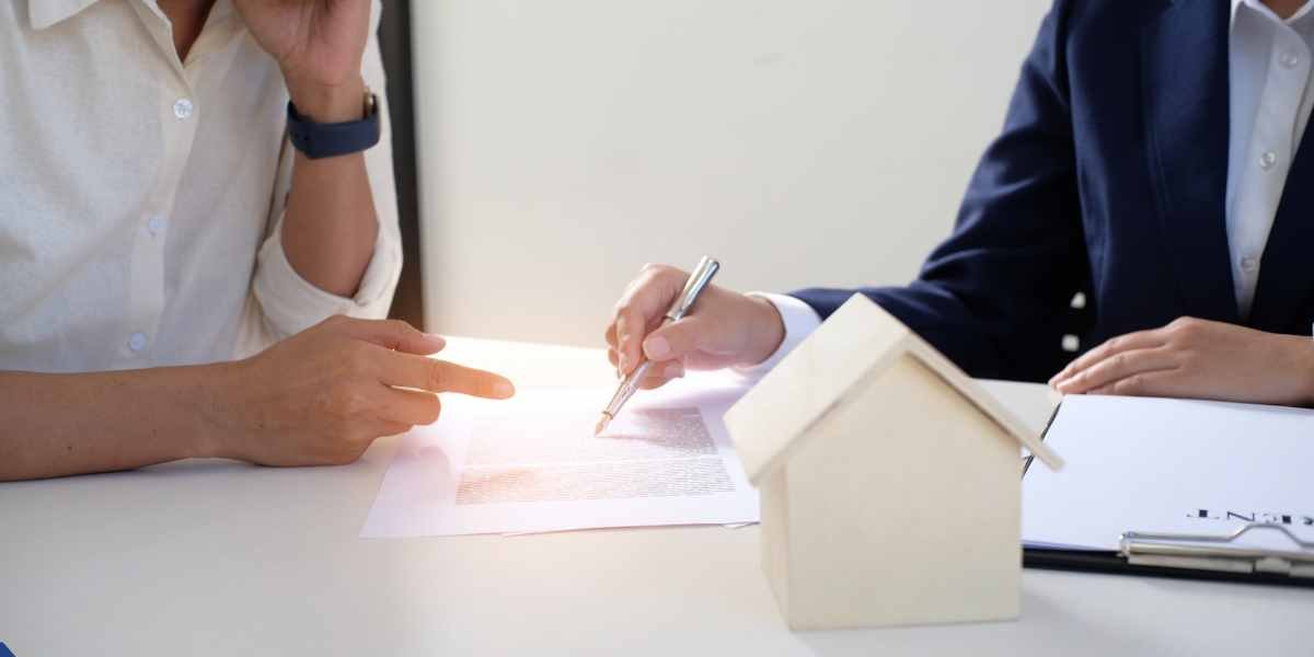 Close-up of a mortgage advisor and client signing a gifted deposit declaration letter with a wooden house model on the desk in the UK.