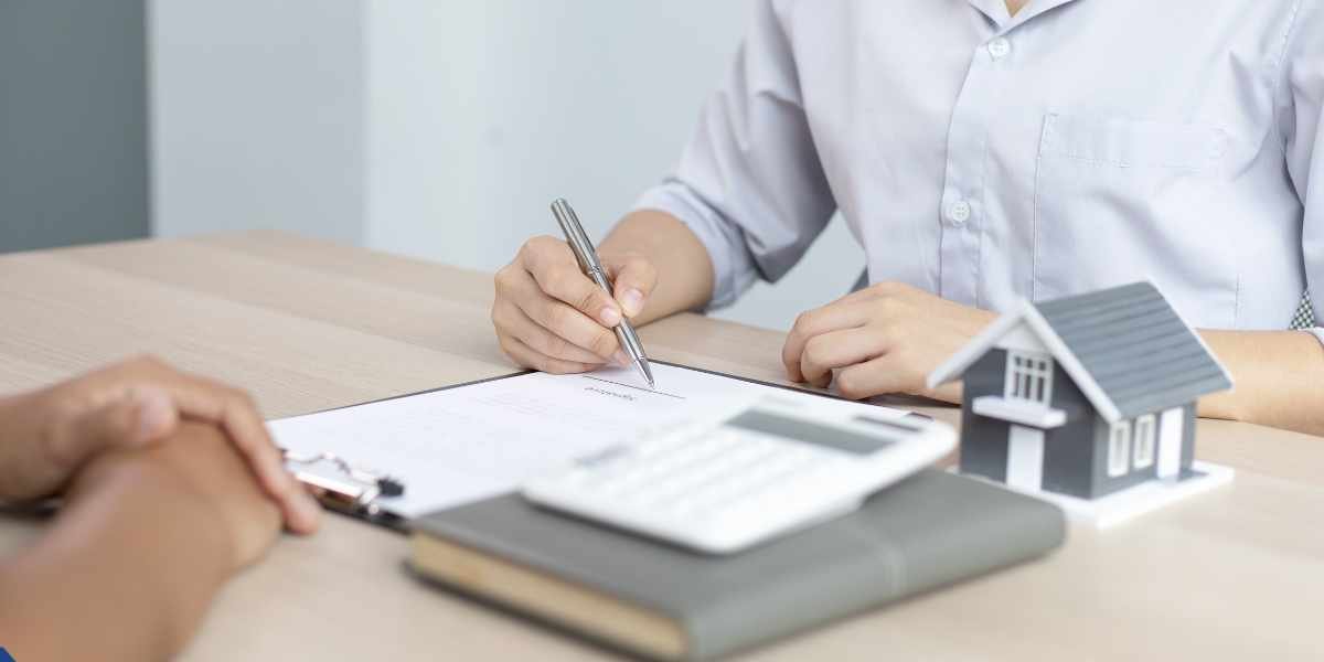 Close-up of a borrower signing loan application documents next to a toy house and calculator, symbolizing the process of getting approved for a mortgage with a poor credit history.