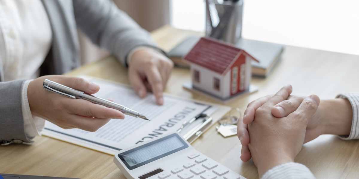An Enfield mortgage broker pointing out details on a financial document to a self-employed applicant, with a calculator and small house model on the desk.